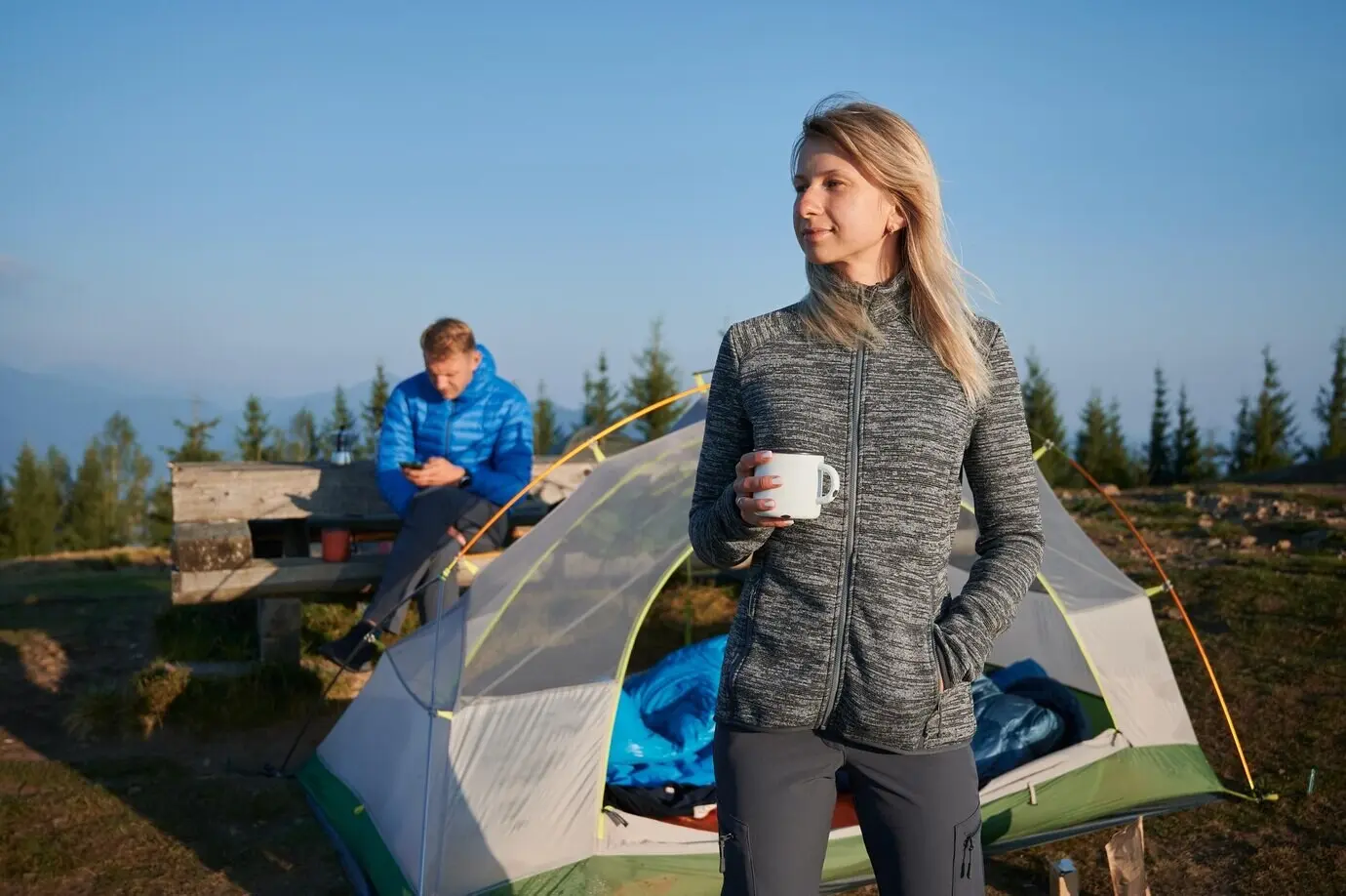 A beautiful young woman and a man relaxing outdoors near a camp tent.