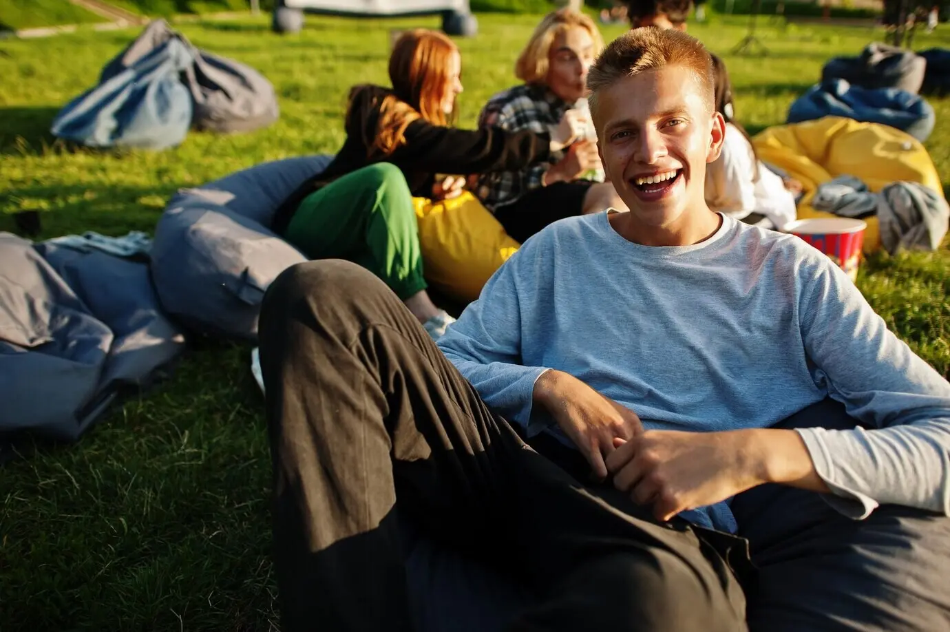 Close-up portrait of a funny guy; a young multi-ethnic group of people watching a movie on a poof at an open-air cinema.